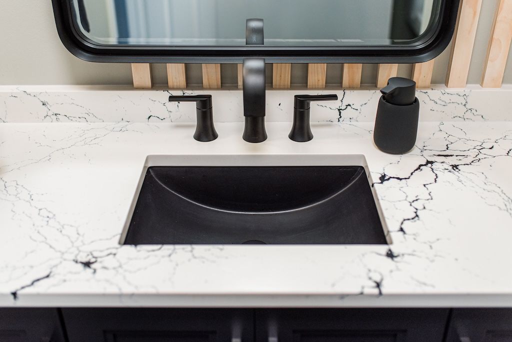Bathroom sink with black fixtures and a black and white countertop, black sink bowl, and black soap dispenser.