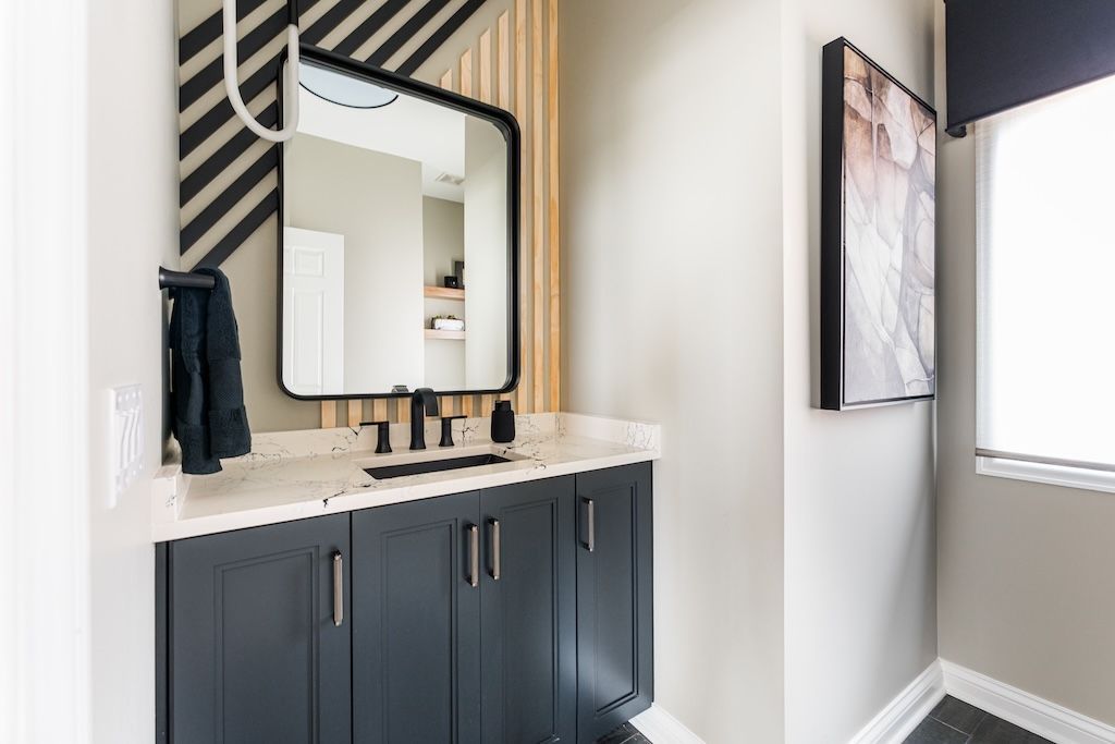Modern bathroom with black vanity, mirror, and striped accent wall.