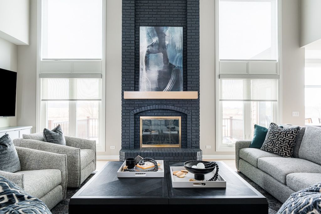 Living room with black painted brick fireplace, artwork, and gray furniture.