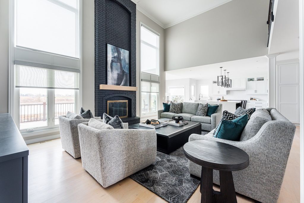 Spacious living room with high ceilings, fireplace, light-colored furniture, and large windows.