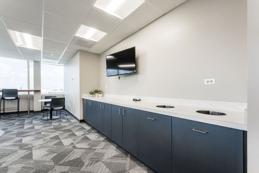 A modern office break room with a TV, cabinets, and a seating area.