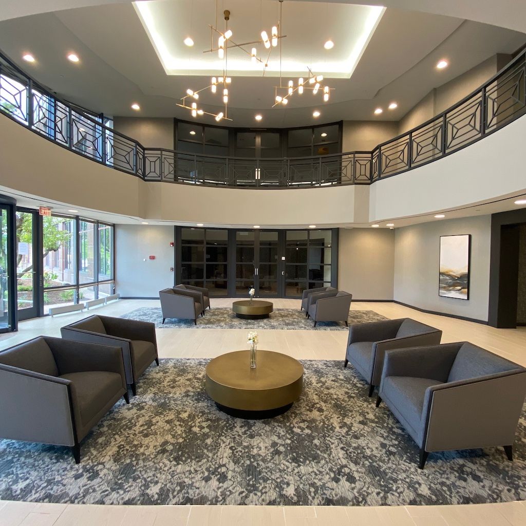 Lobby with seating area, two-story, large windows, chandelier, black railings, neutral tones, gray armchairs around coffee tables.