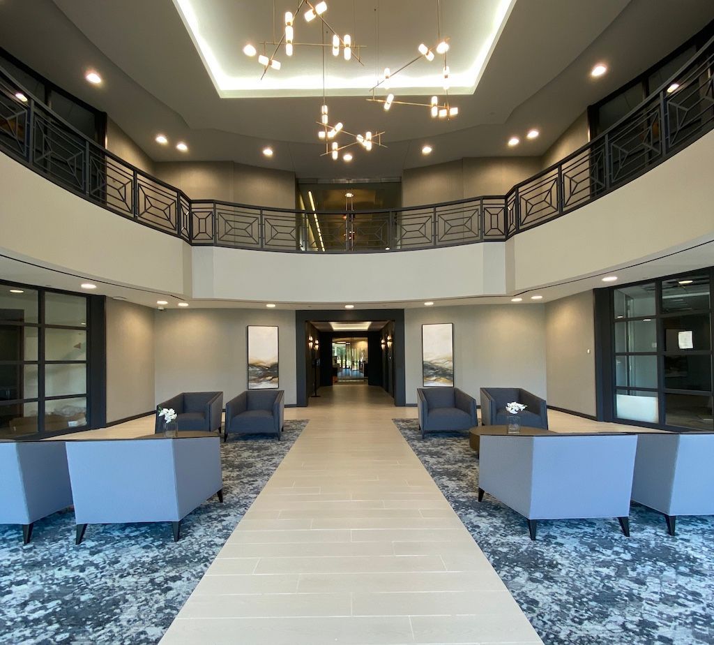 Lobby with seating, neutral colors, modern chandelier, and a balcony above.