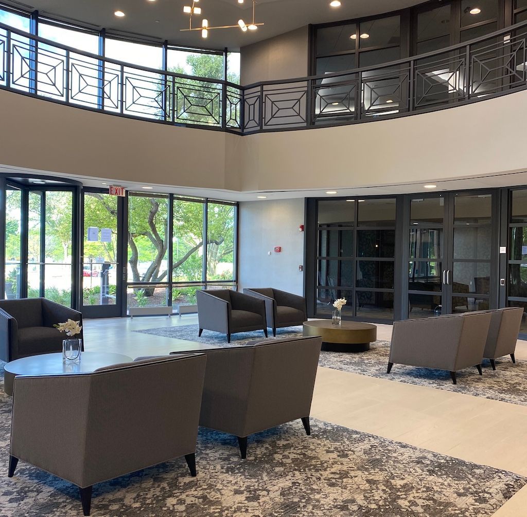 Lobby with gray furniture, large windows, and a second-story railing.