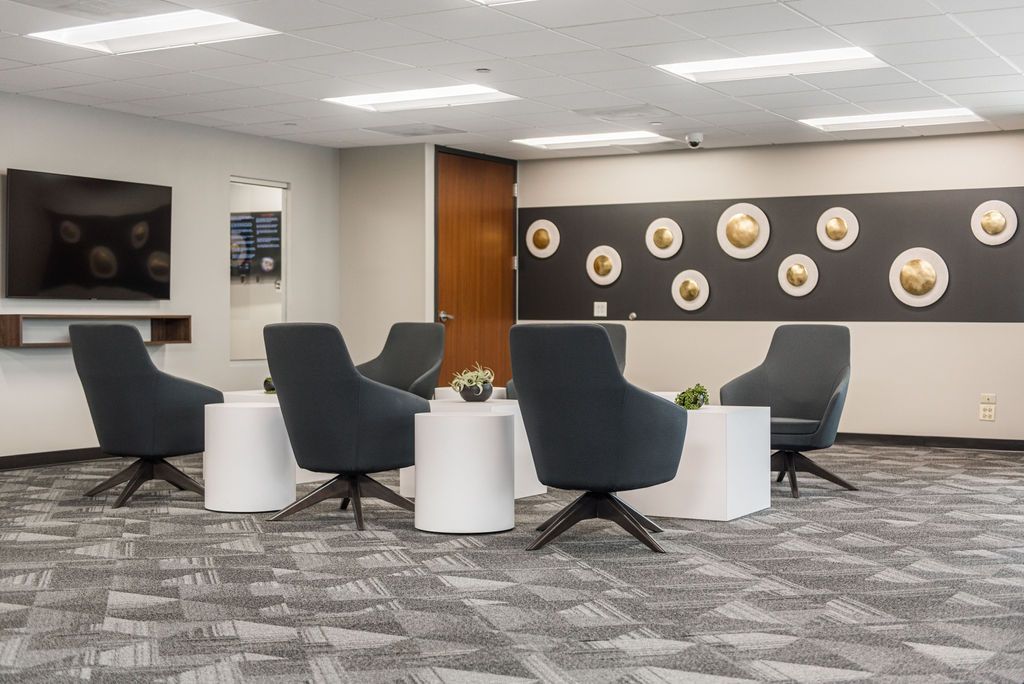 Lounge area with gray chairs, white tables, and patterned carpet. A TV and decorative wall art are visible.
