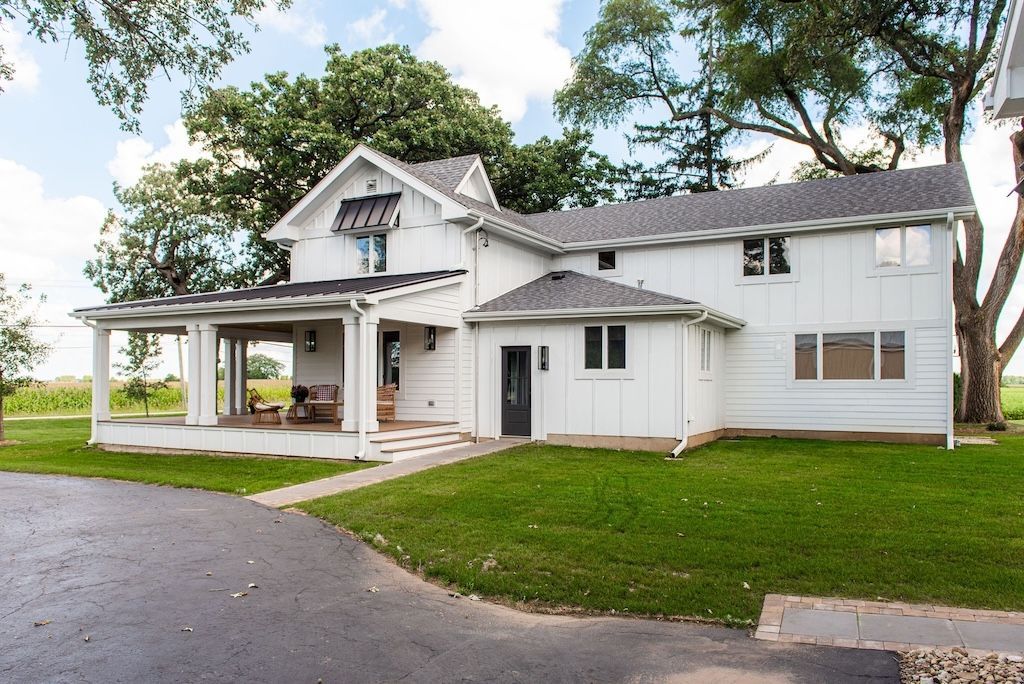 White farmhouse with porch, black awning, and green lawn.