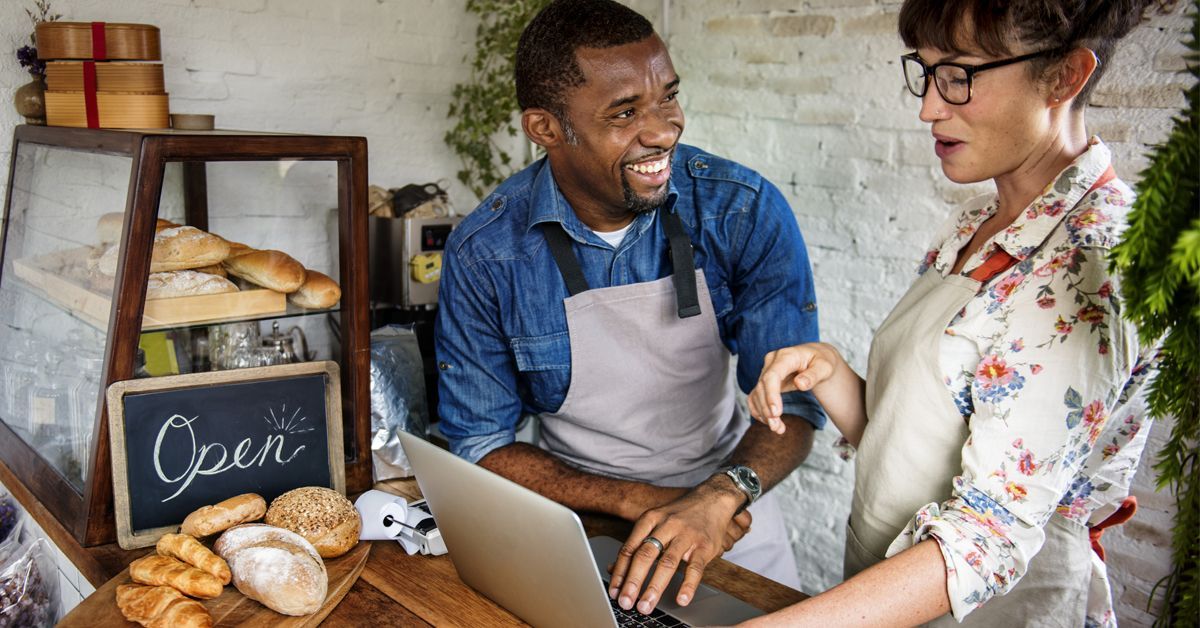 A man and a woman are looking at a laptop in a bakery.