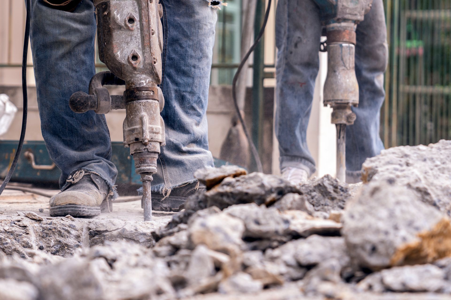 Worker using jackhammer to break concrete slab during demolition at construction site. Worker using jackhammer to break concrete slab during demolition at construction site.