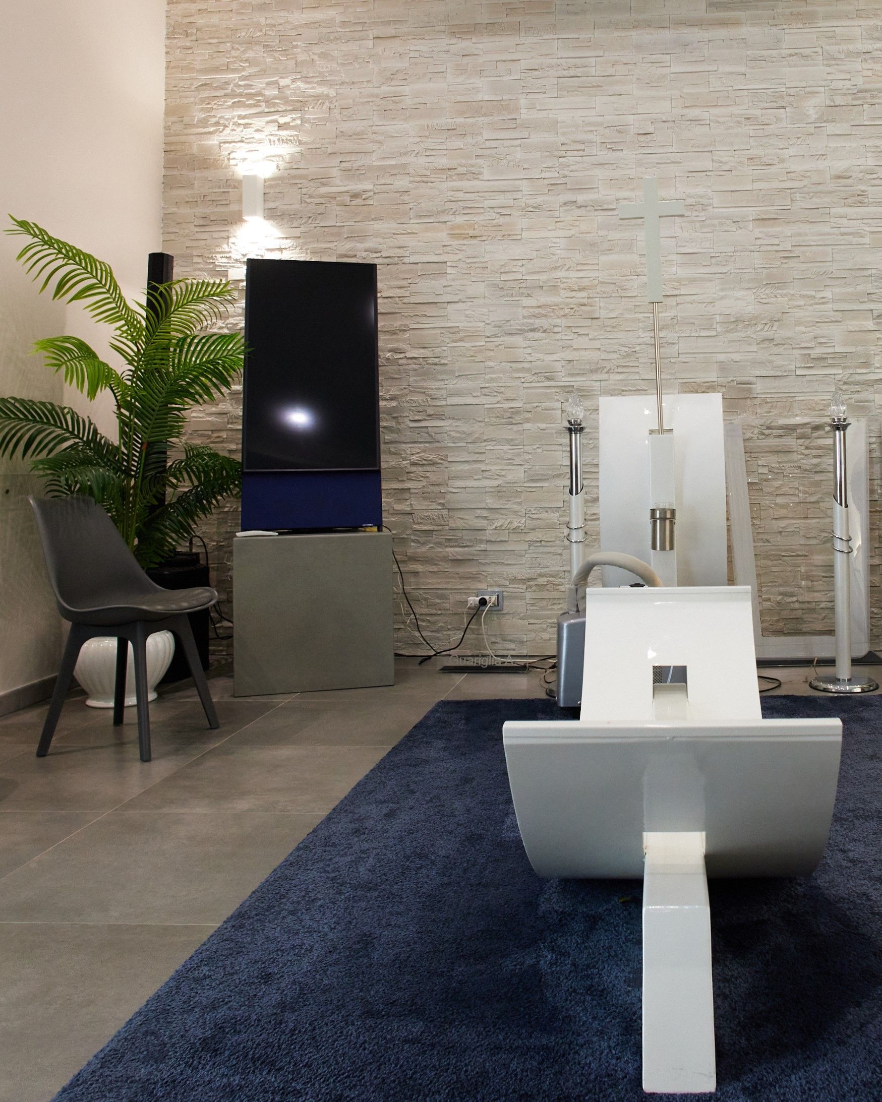 Soggiorno moderno con grande TV, altoparlanti bianchi e tappeto blu.