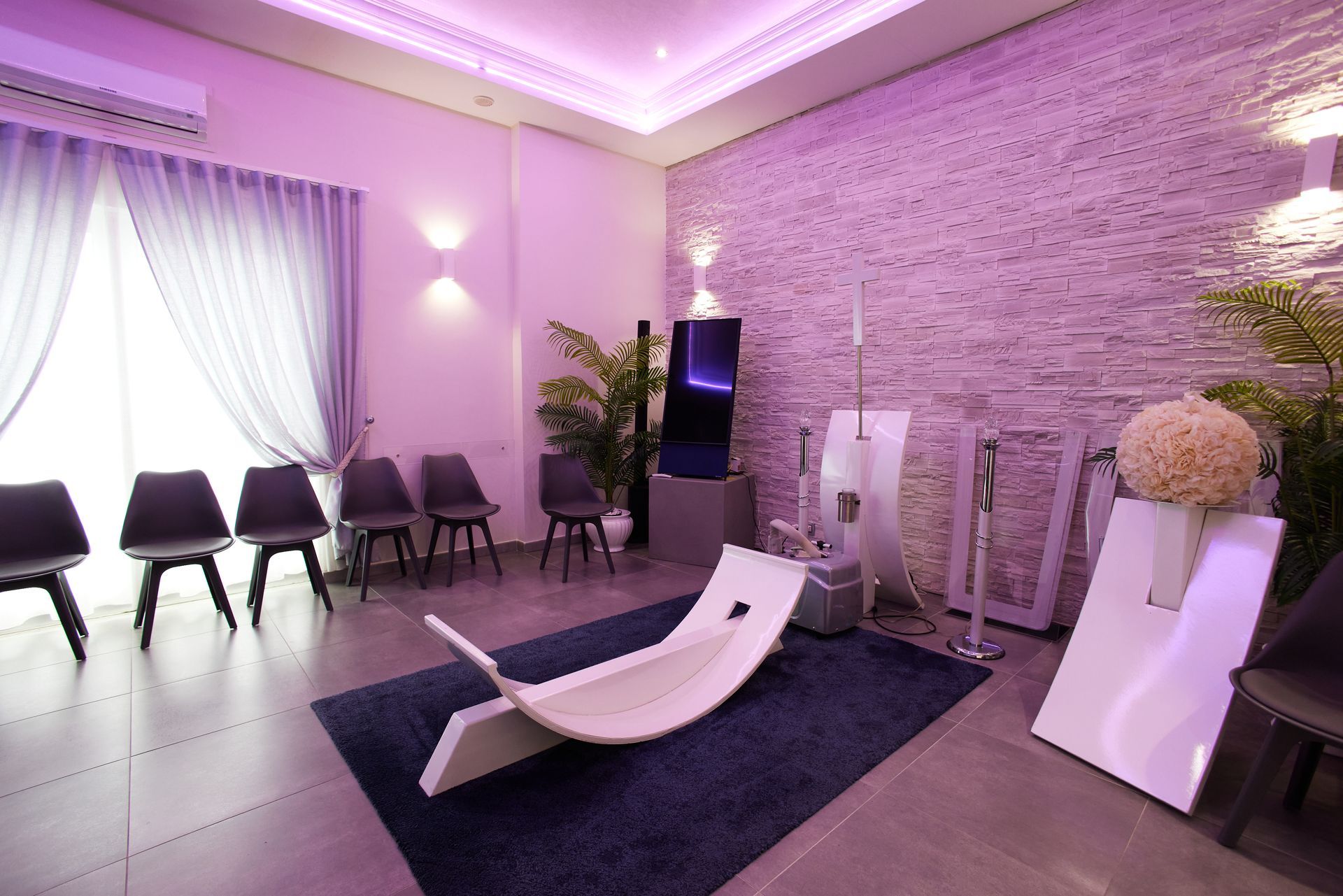 Una sala d'attesa con sedie, una panca curva ed elementi decorativi illuminati da luci viola.