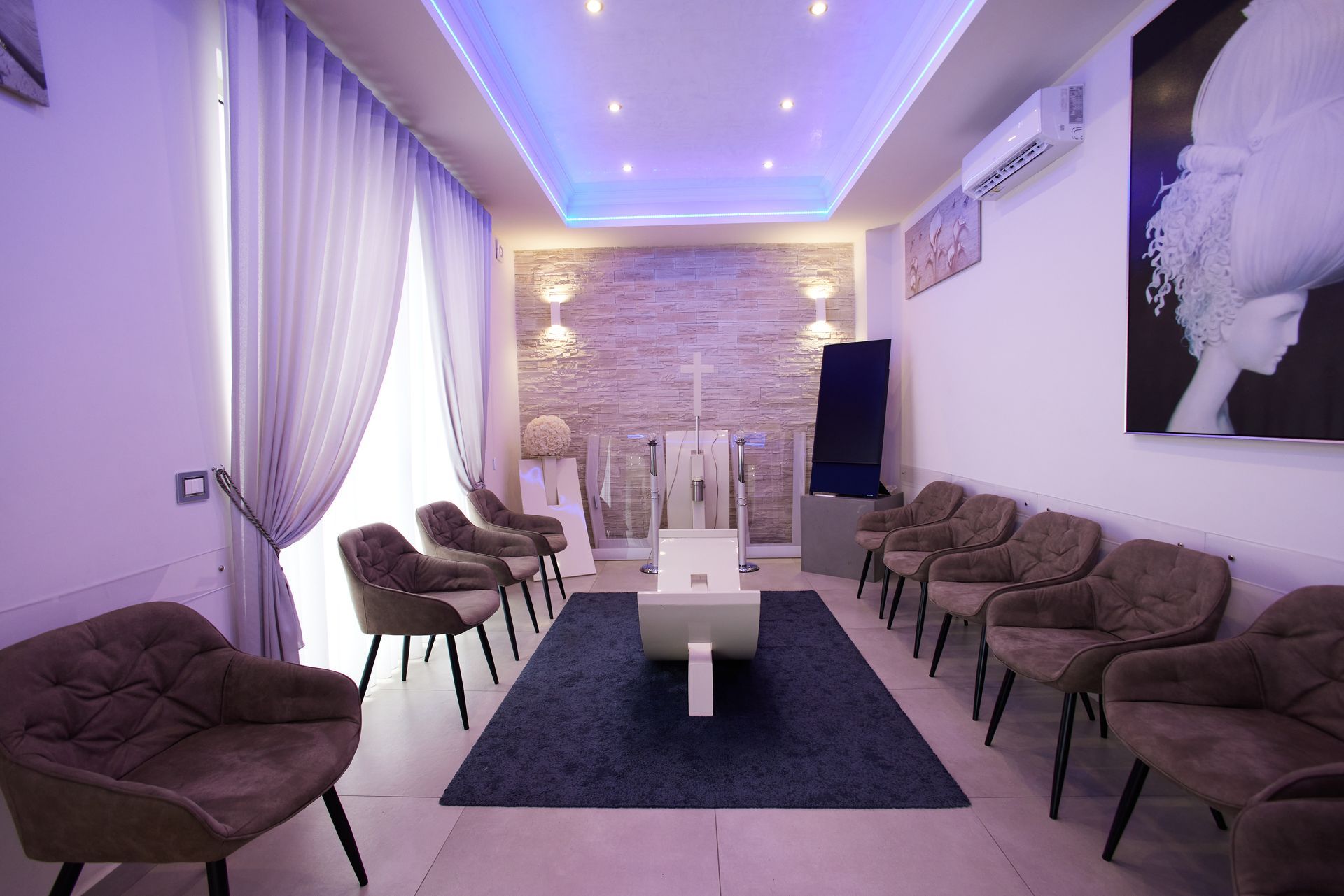 Sala d'attesa con comode poltrone marroni, un tappeto blu e un arredamento moderno con illuminazione ambientale.