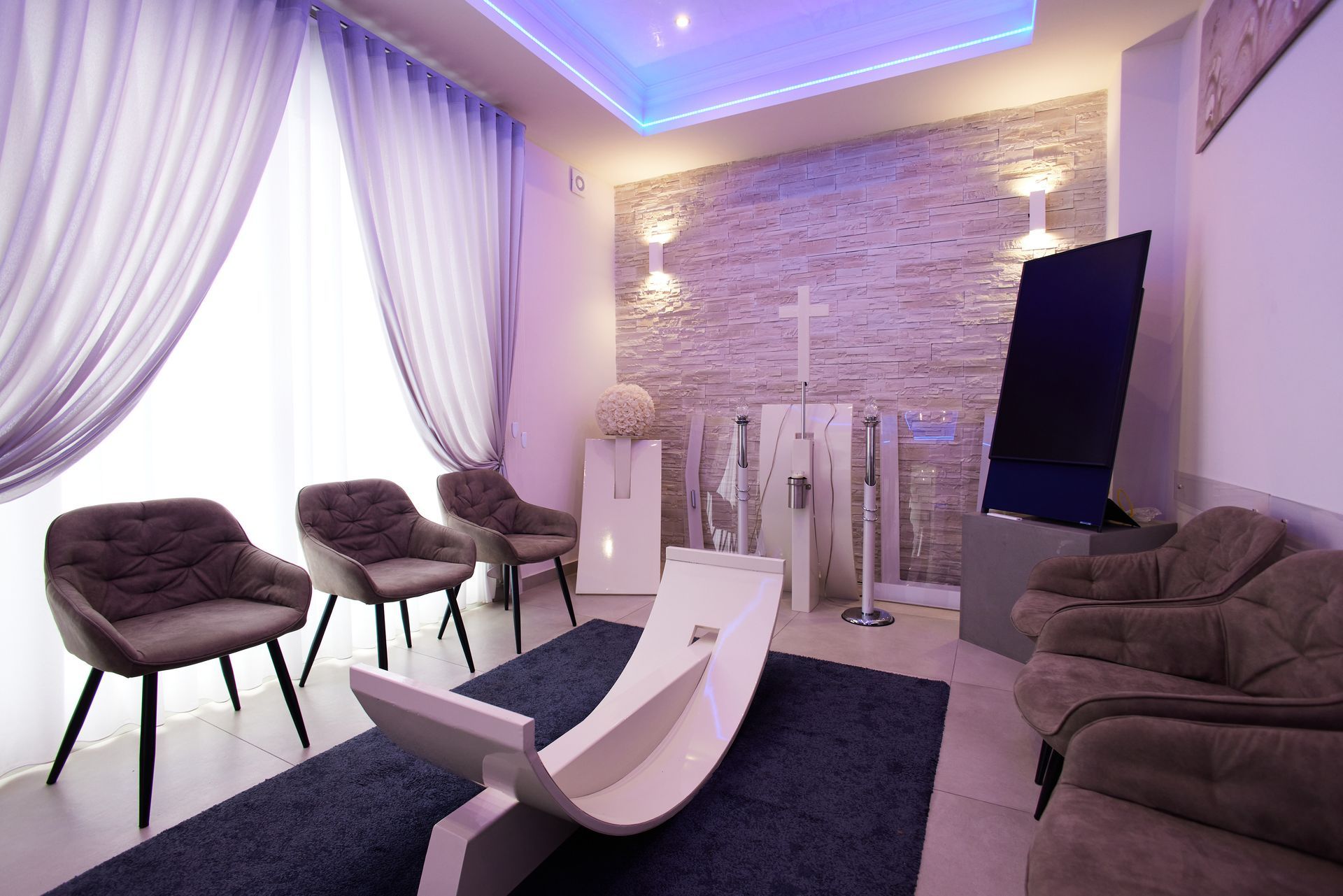 Interno di un'agenzia di pompe funebri con sedie, croce, TV e illuminazione decorativa.