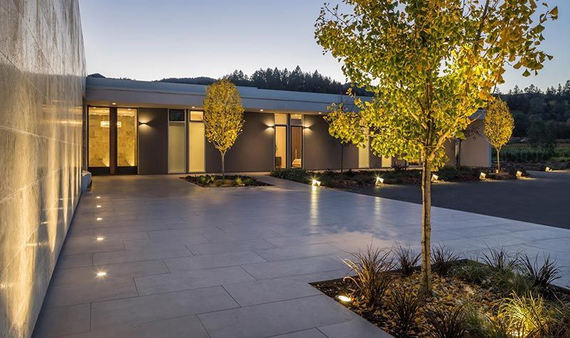 Exterior of modern building with lit walkways and trees. Evening.