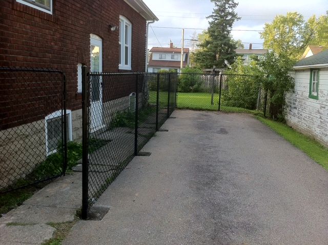 A chain link fence surrounds a driveway in front of a brick house