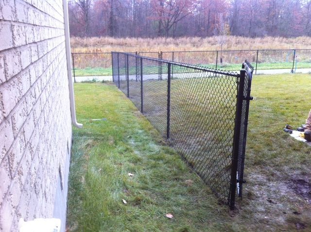 A chain link fence is surrounding a grassy yard next to a brick building.
