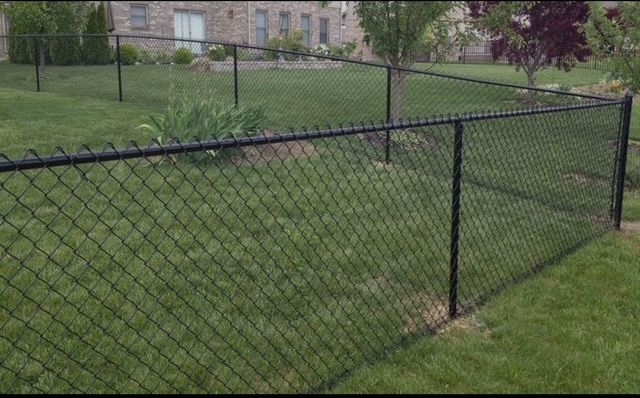A chain link fence is in the middle of a lush green yard.