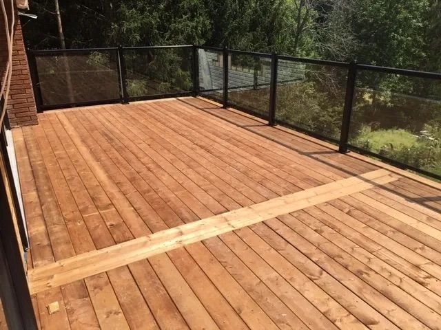 A wooden deck with a glass railing and trees in the background.
