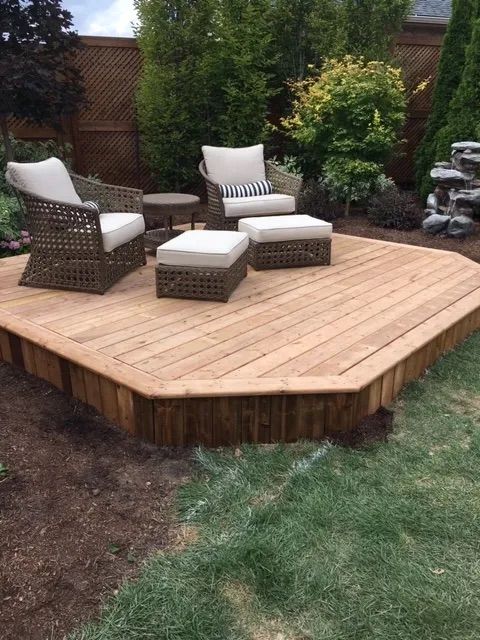 A wooden deck with chairs and ottomans in a backyard.