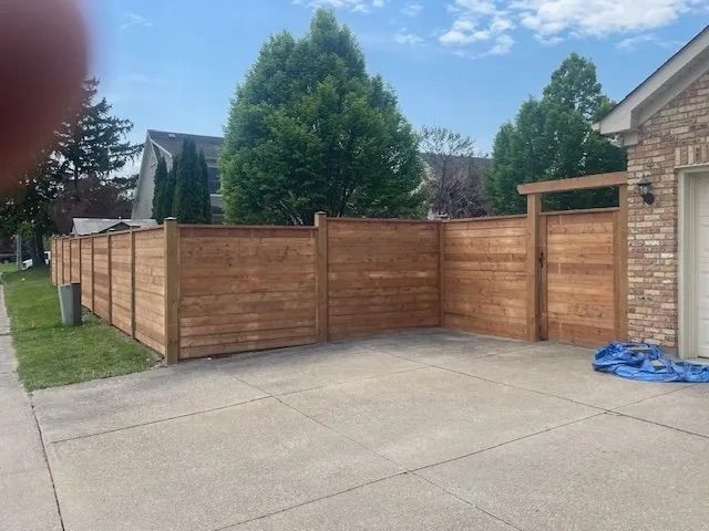 A wooden fence is surrounding a driveway in front of a brick house.