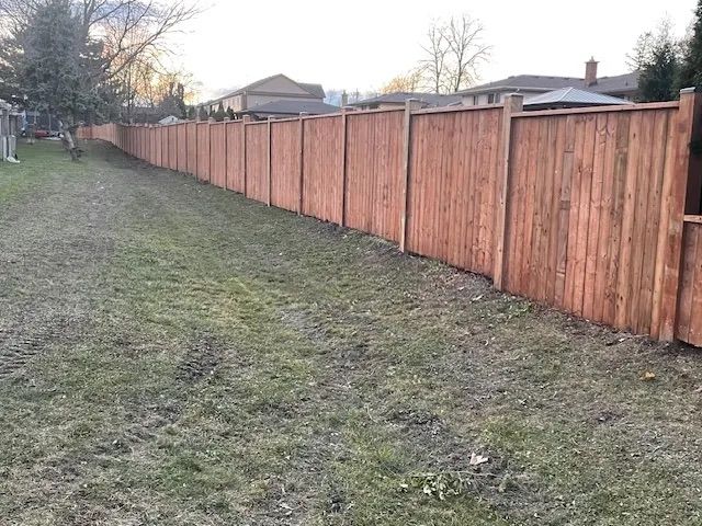 A long wooden fence surrounds a grassy yard in a backyard.