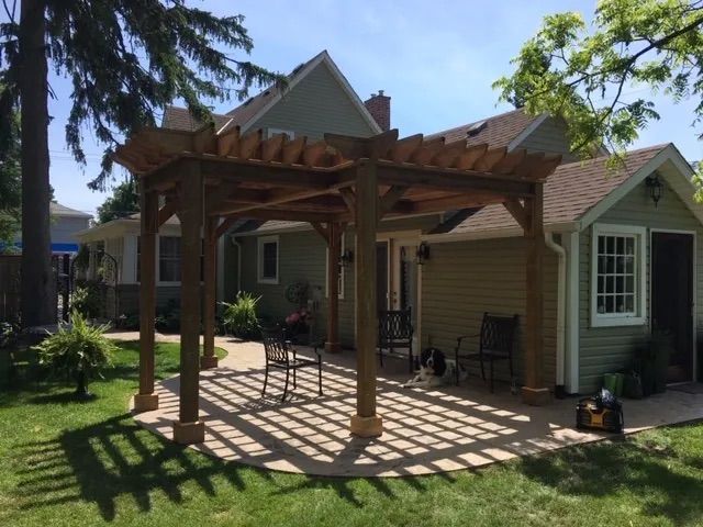 A wooden pergola is in the backyard of a house.