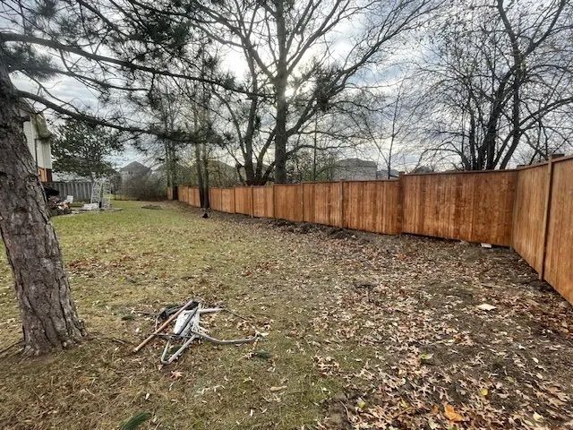 A wooden fence surrounds a lush green yard with trees in the background.