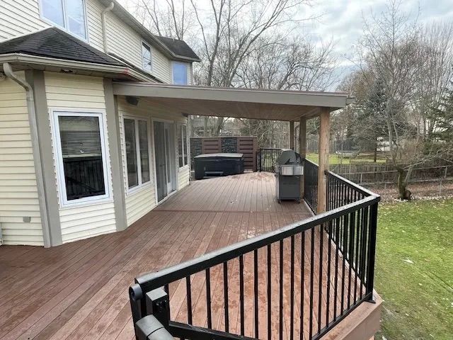 A large wooden deck with a black railing and a hot tub underneath it.