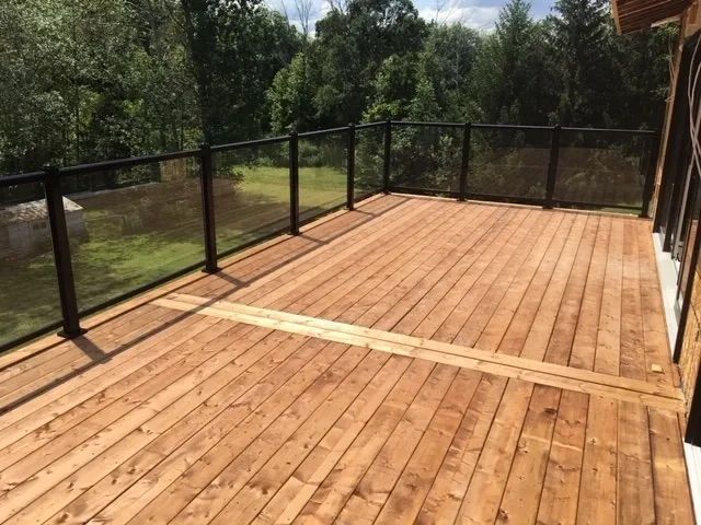 A large wooden deck with a glass railing and trees in the background.