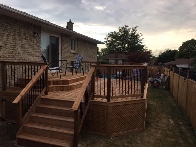 A wooden deck with stairs leading up to it is in the backyard of a house.