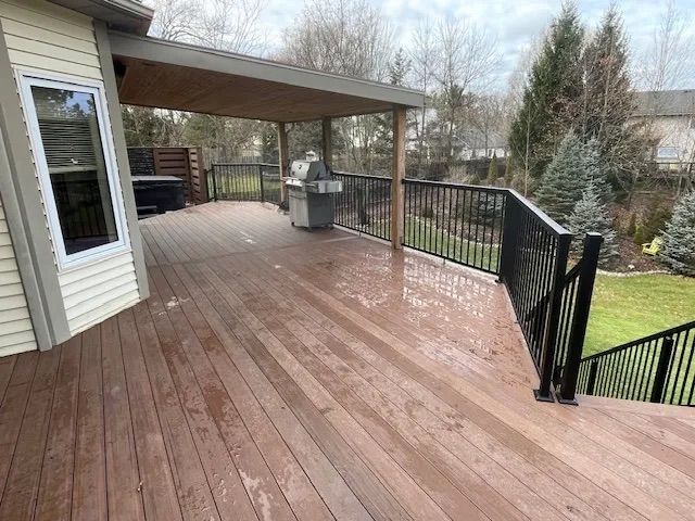 A large wooden deck with a grill and stairs leading up to it.