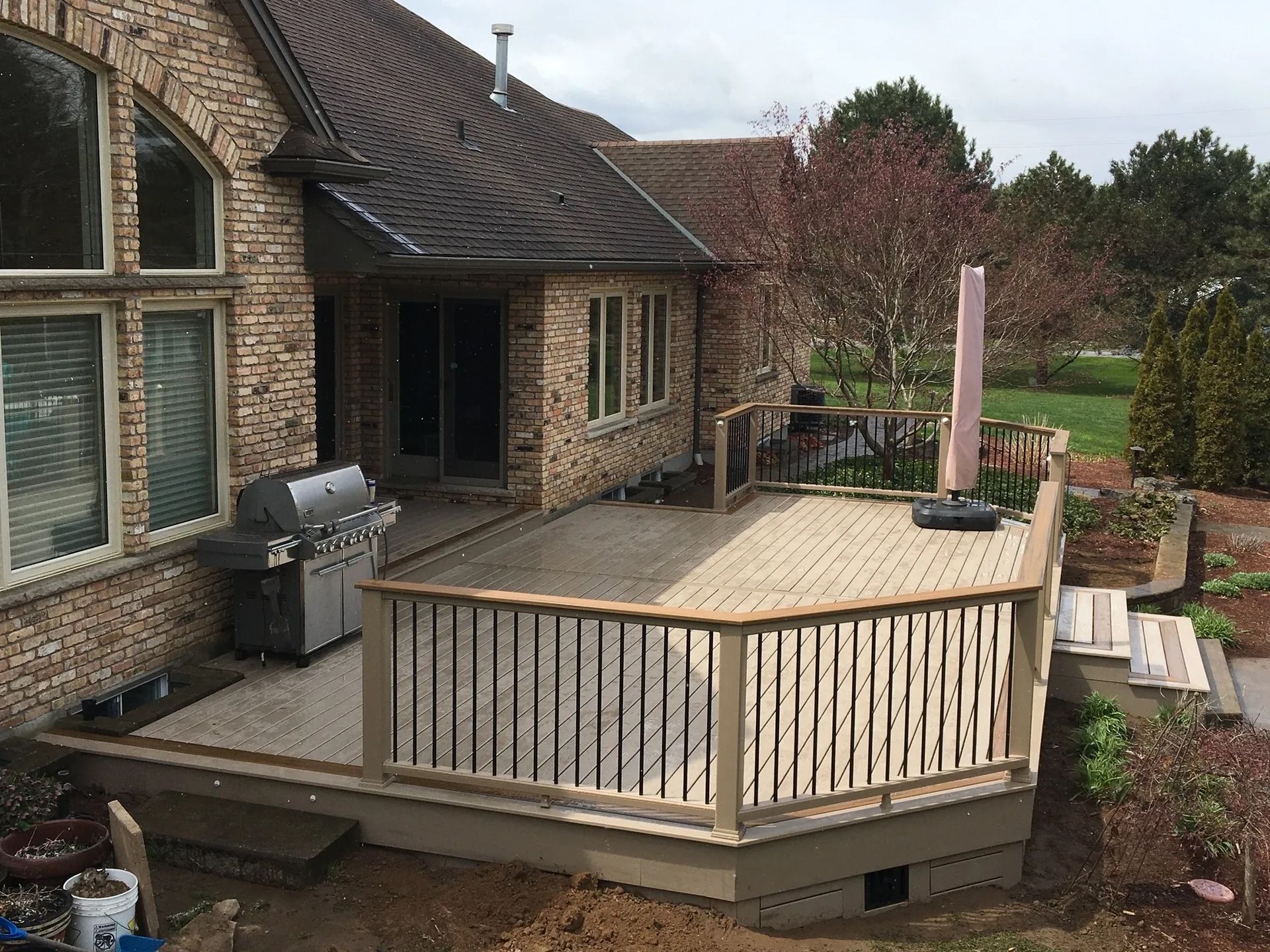 A large wooden deck with a grill on it in front of a brick house.