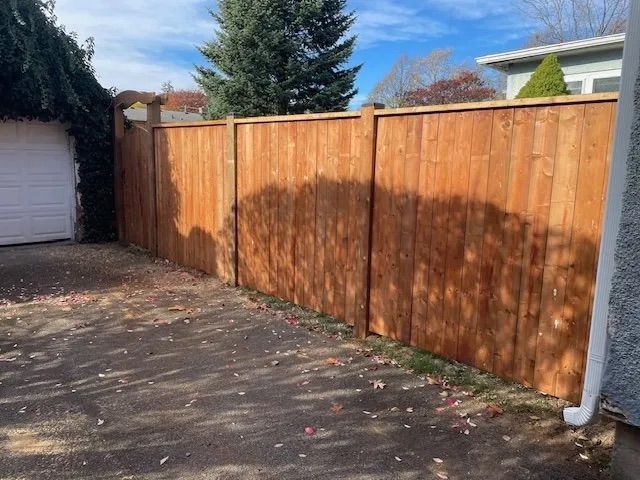 A wooden fence surrounds a driveway next to a garage.
