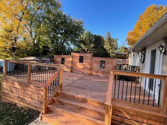 A large wooden deck with stairs leading up to it is in front of a house.
