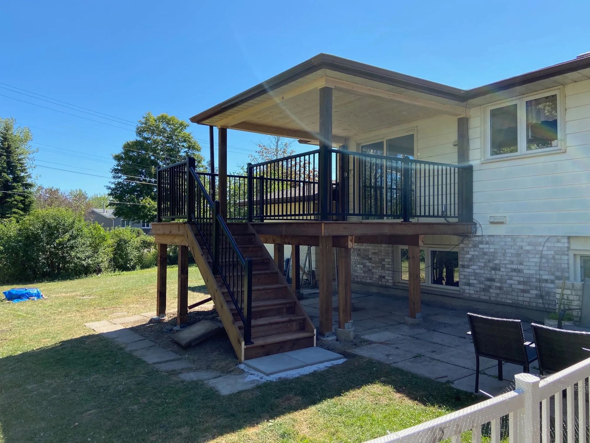 A large deck with stairs leading up to it is in the backyard of a house.