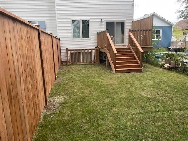 A wooden fence surrounds a backyard with a deck and stairs.