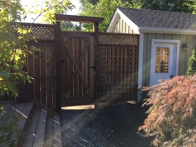 A wooden gate leading to a shed with a white door