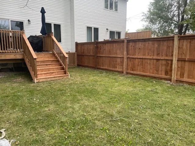 A backyard with a wooden fence and stairs leading to a deck.