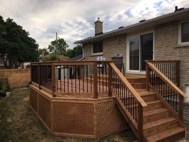 A wooden deck with stairs leading up to it in front of a brick house.