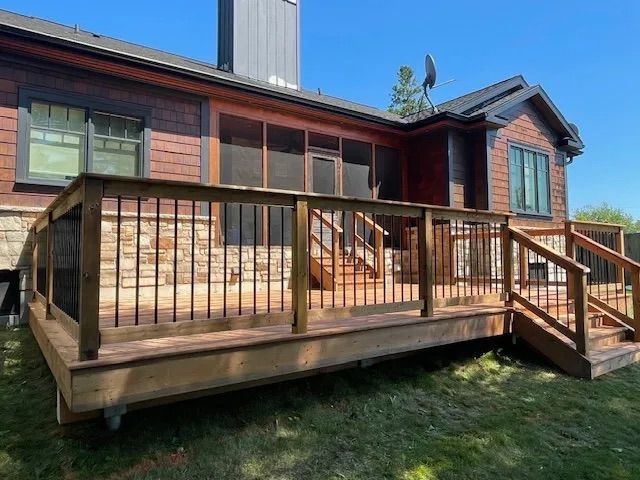 A large wooden deck with stairs is in front of a house.