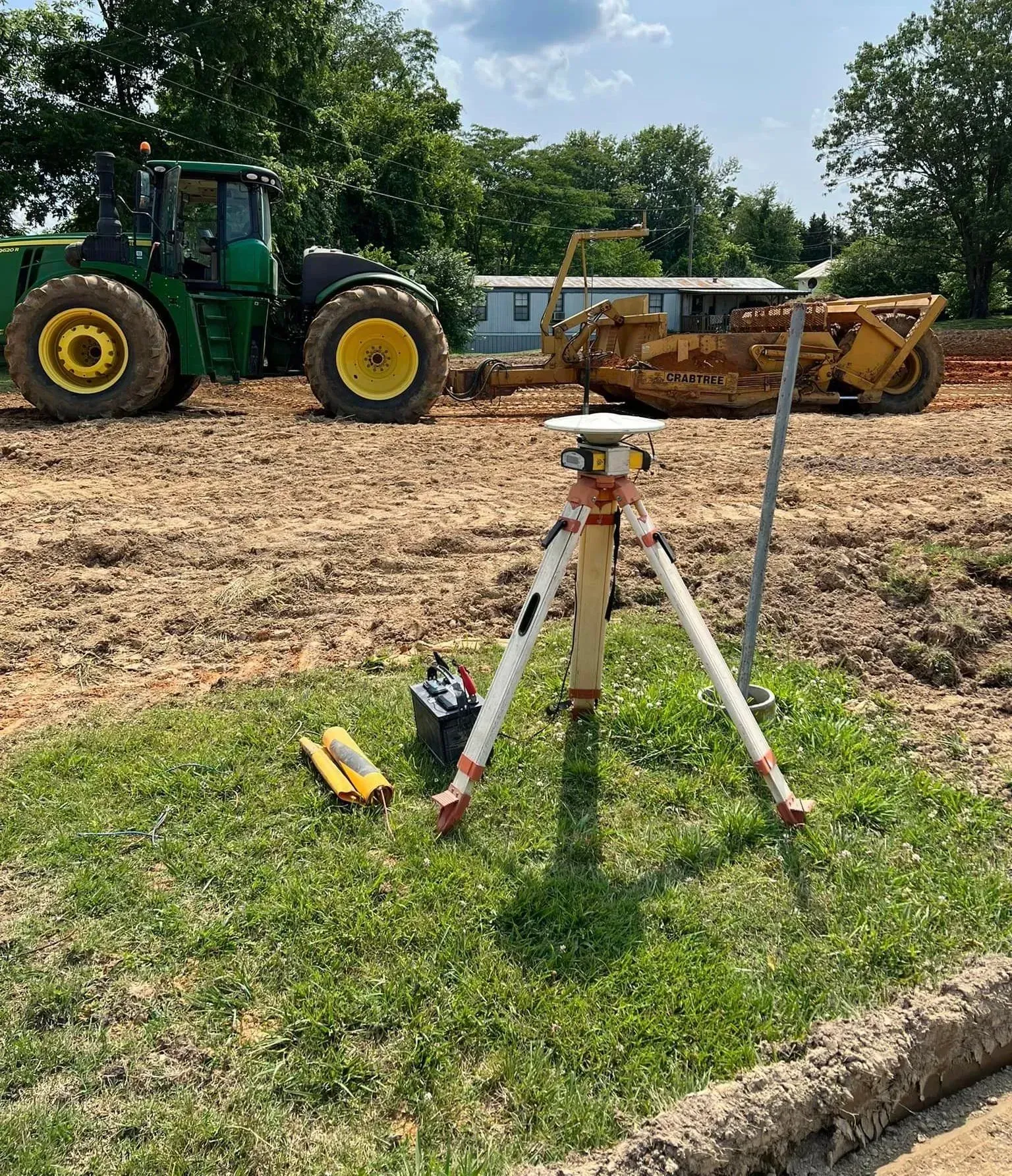 A tripod is sitting in the grass next to a tractor and a bulldozer.