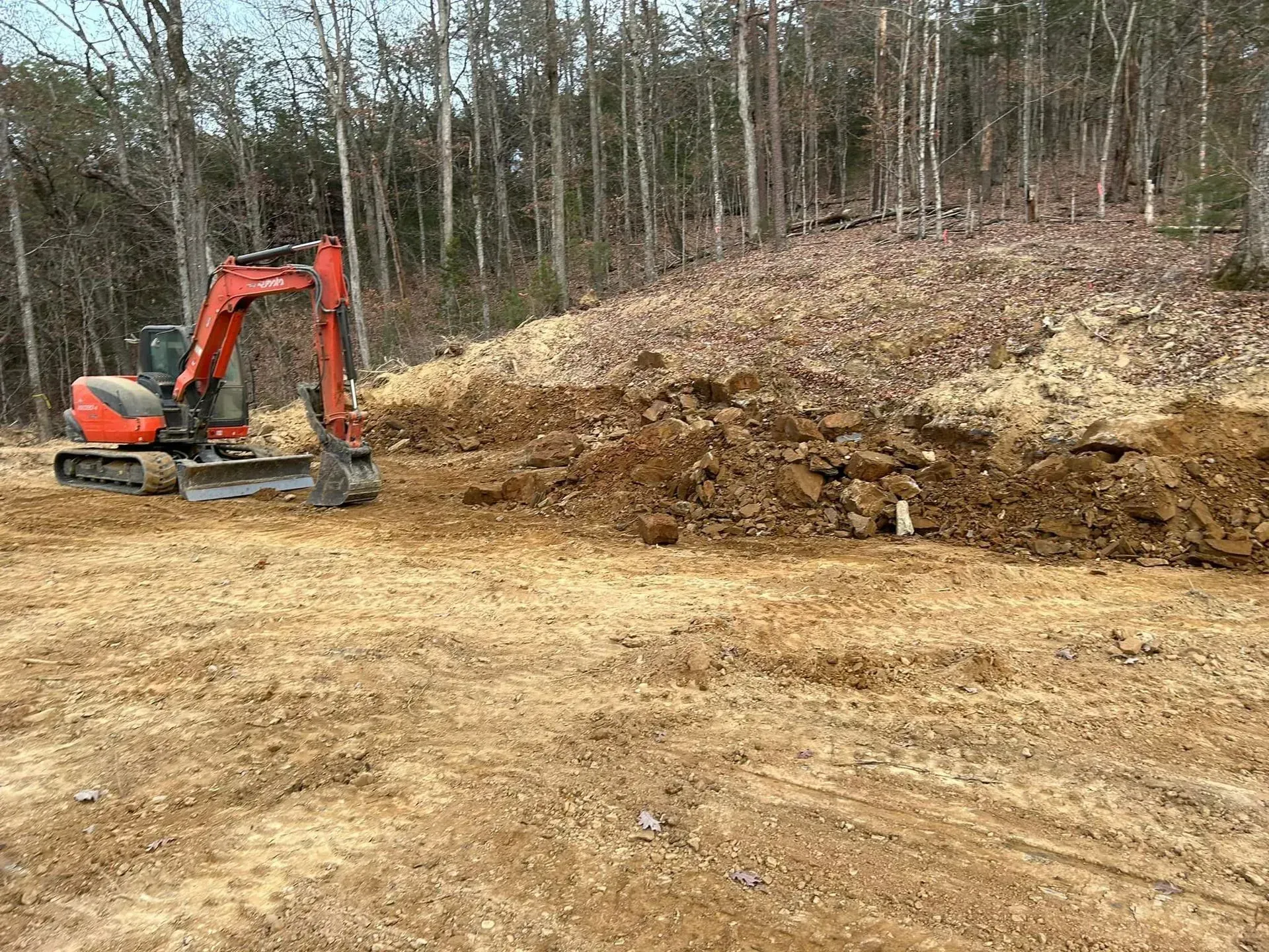 An excavator is moving dirt in a field with trees in the background.