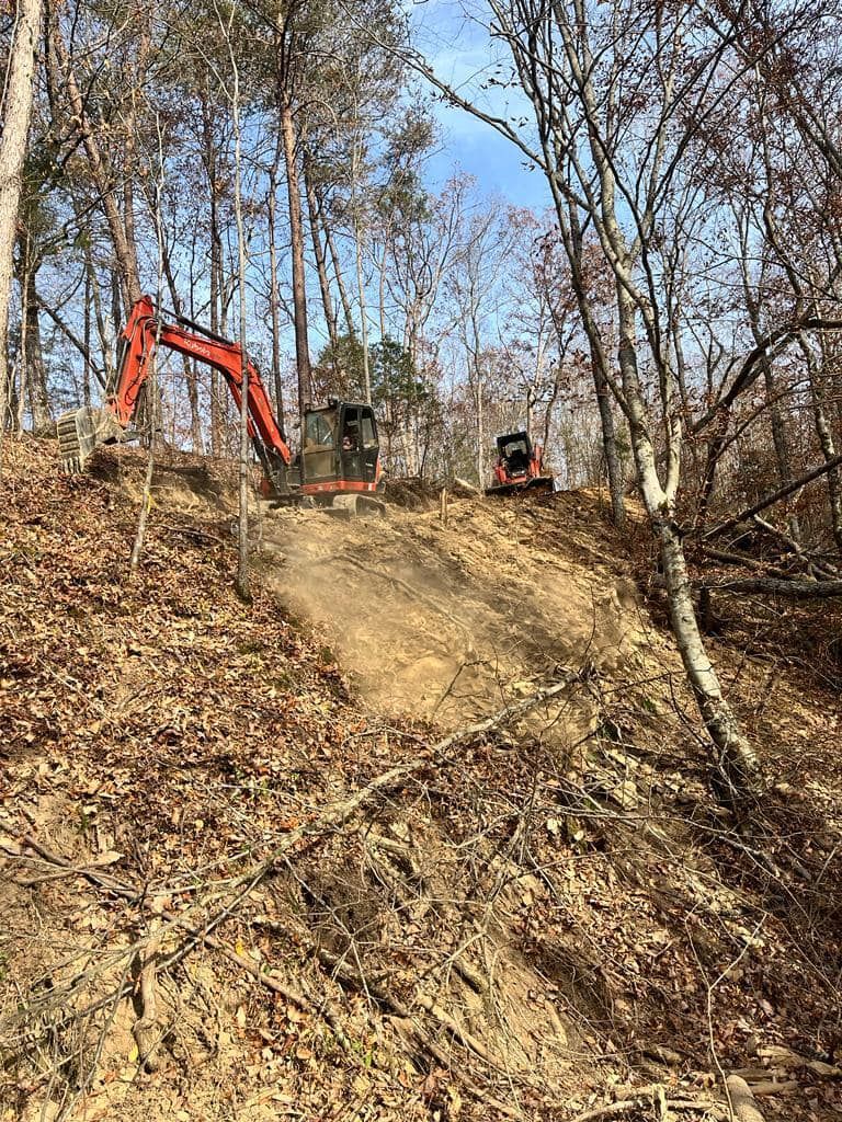 An excavator is driving down a dirt road in the woods.
