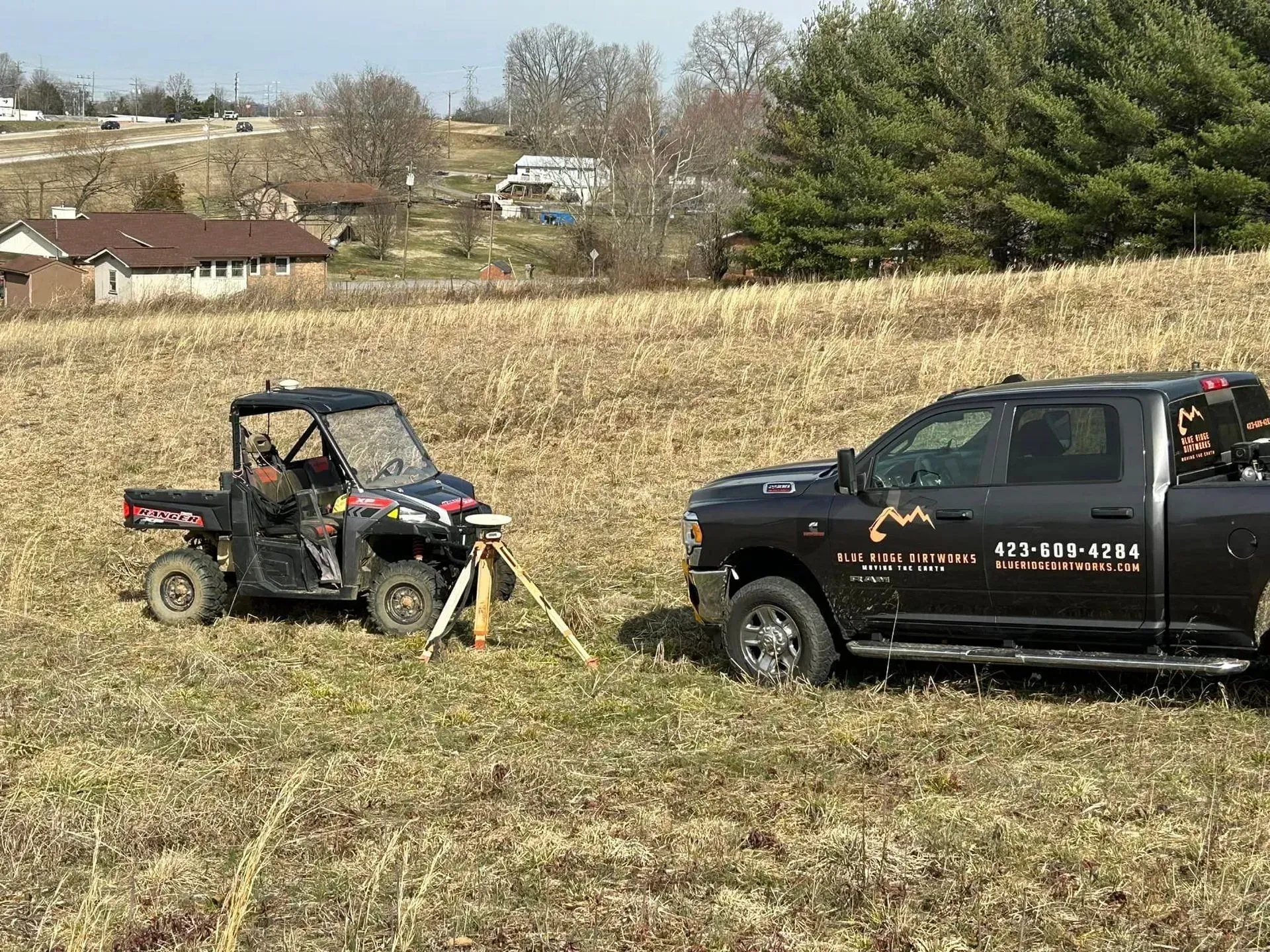 A truck and a atv are parked in a field.