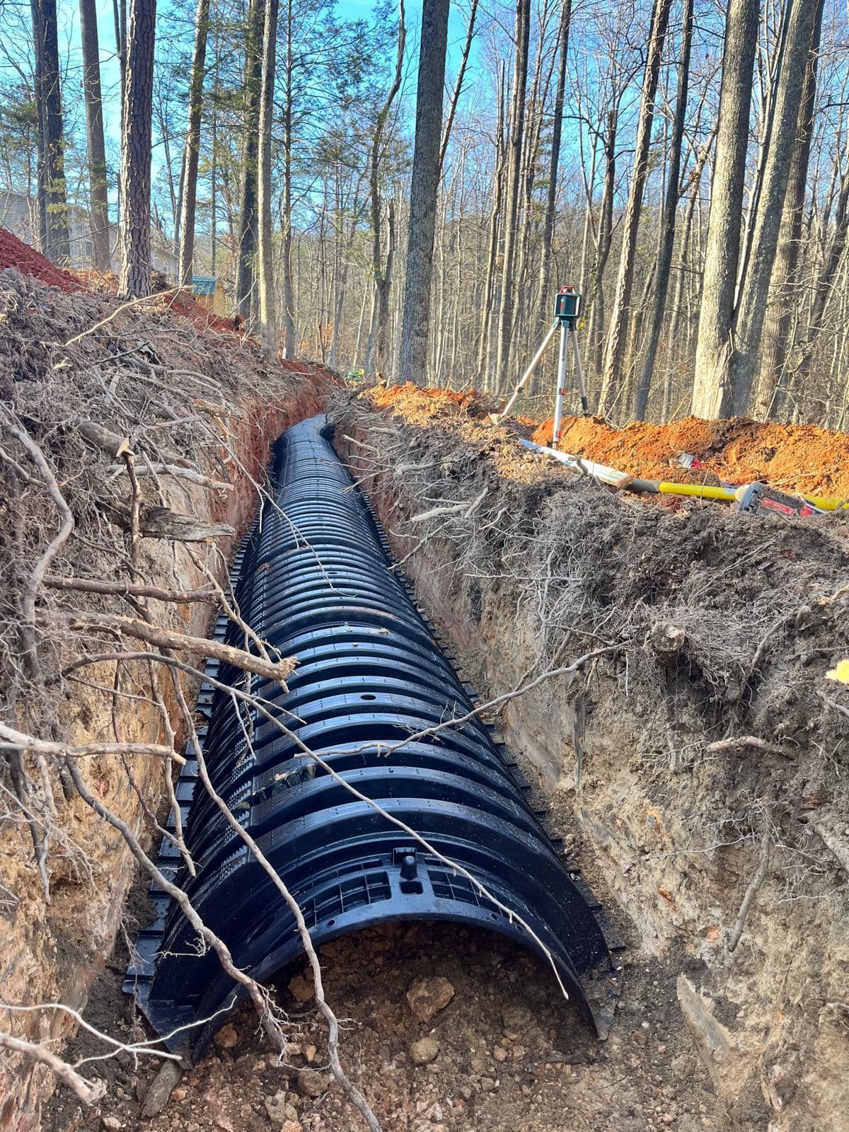 A large pipe is being installed in a trench in the woods.