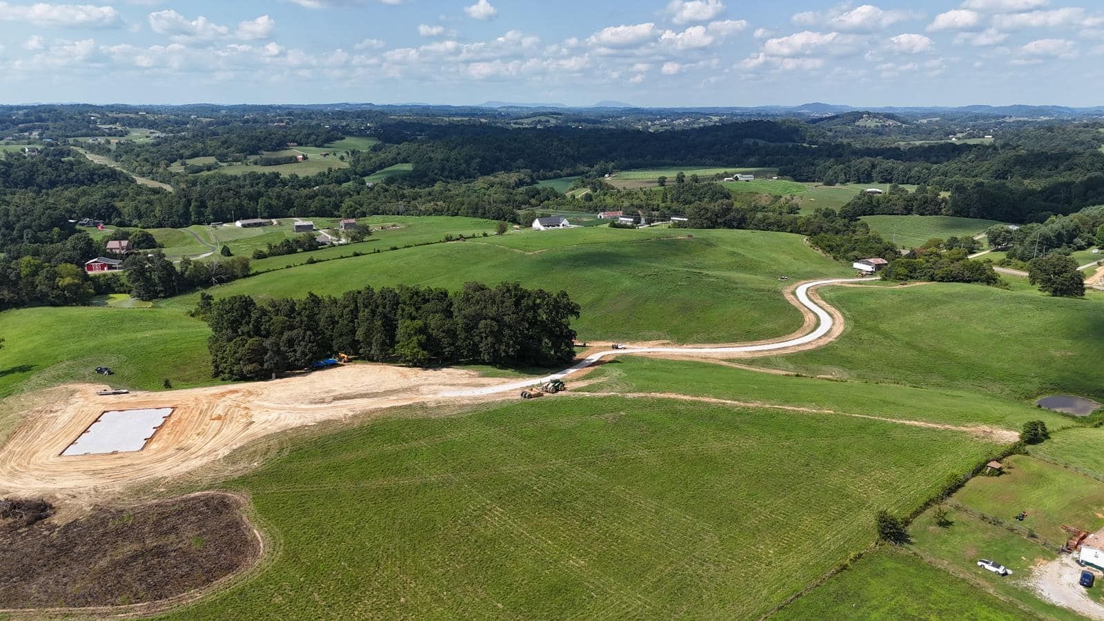 An aerial view of a lush green field with trees and a road.