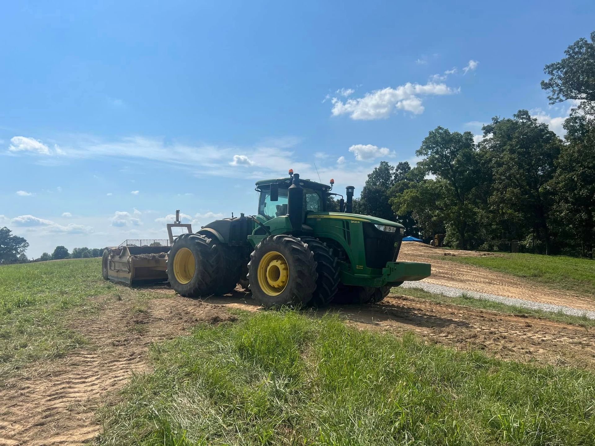 A green tractor is driving down a dirt road in a field.