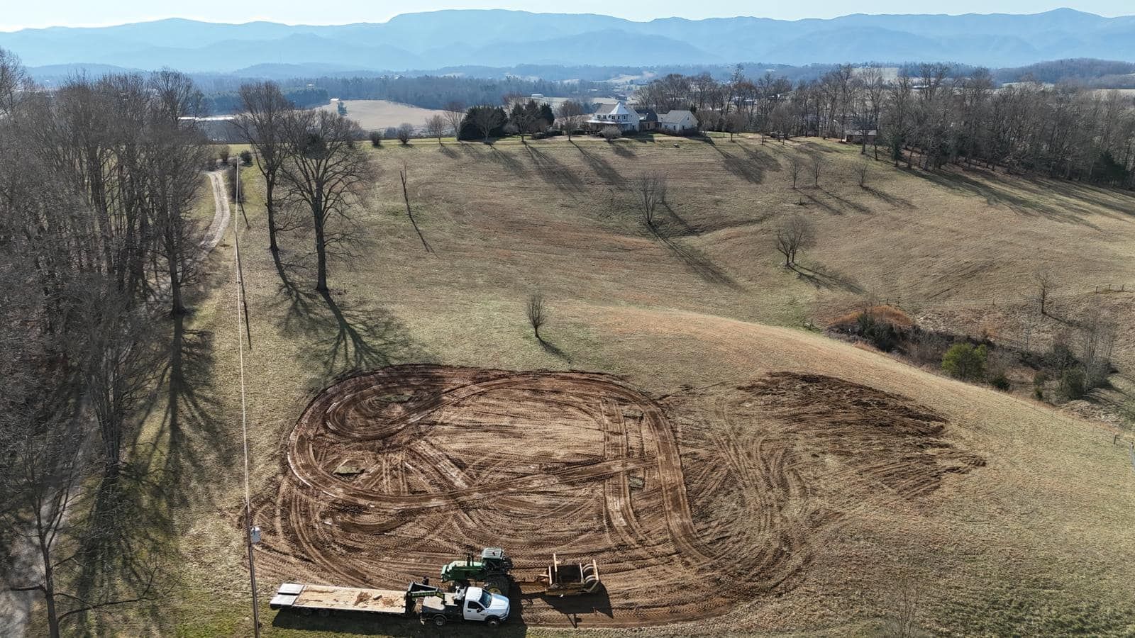 An aerial view of a tractor plowing a field with mountains in the background.