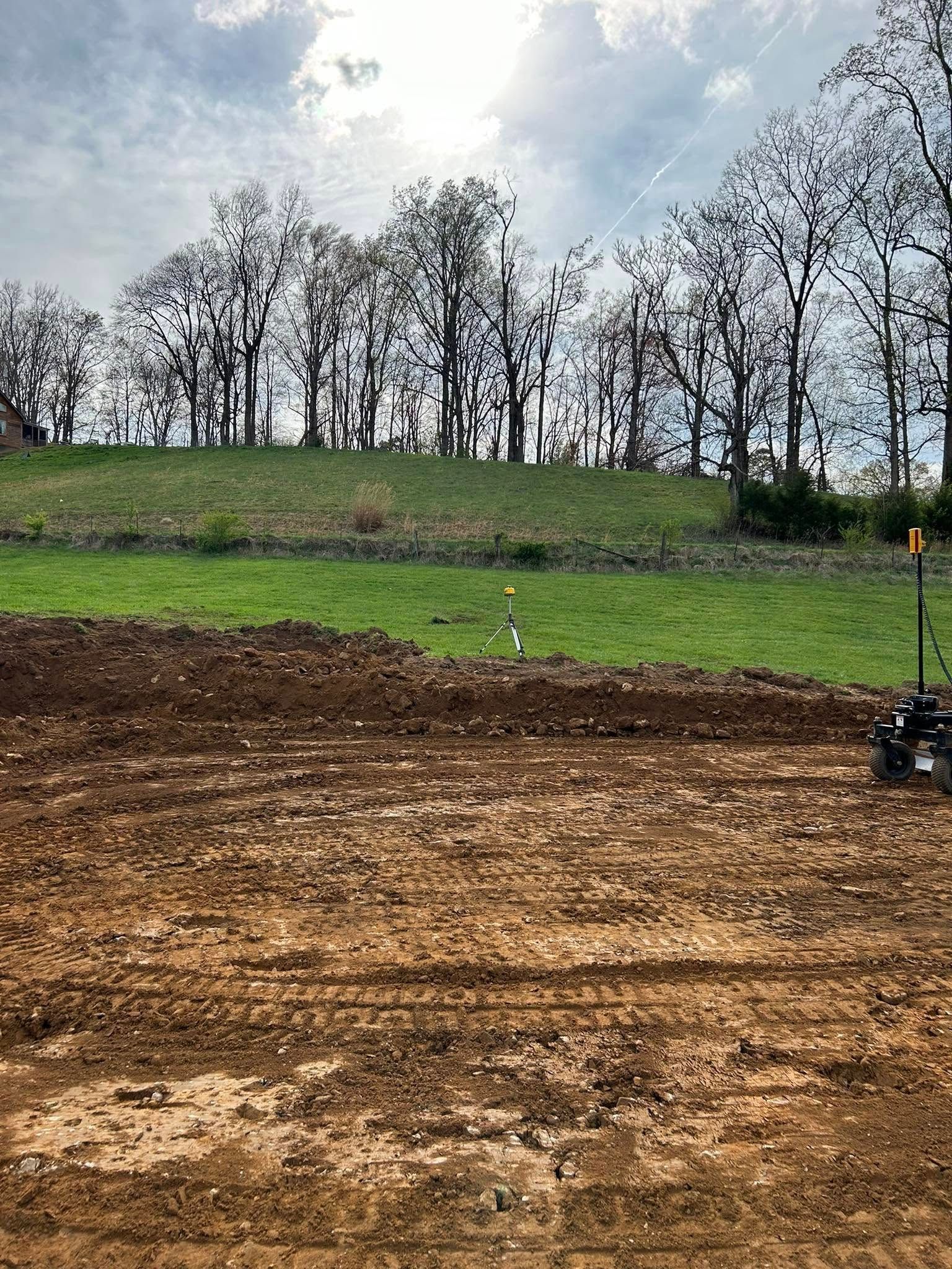 A dirt field with trees in the background and a tractor in the foreground.
