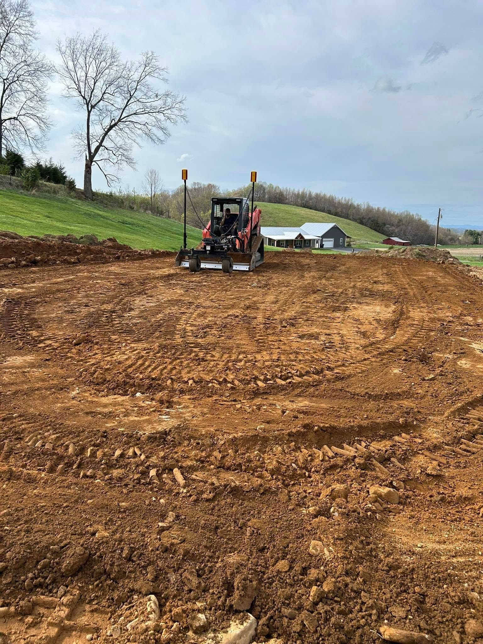 A tractor is plowing a dirt field with a house in the background.
