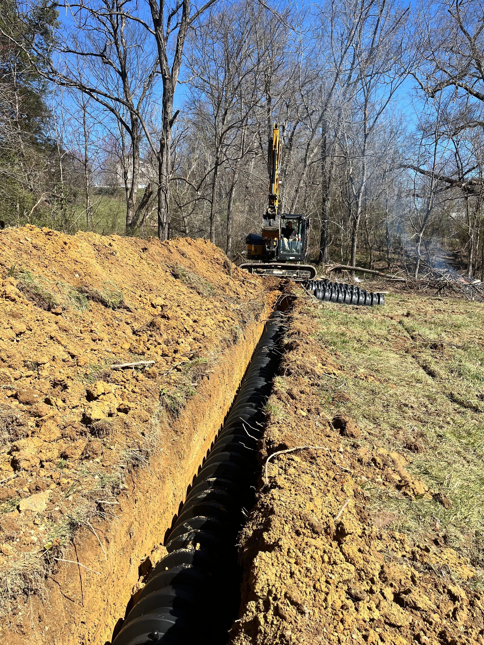 A large excavator is digging a trench in the dirt in a field.
